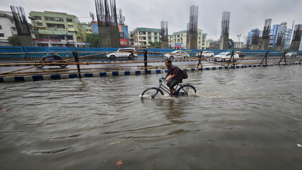 Mann fährt mit Fahrrad durch Wasser auf einer überfluteten Straße.