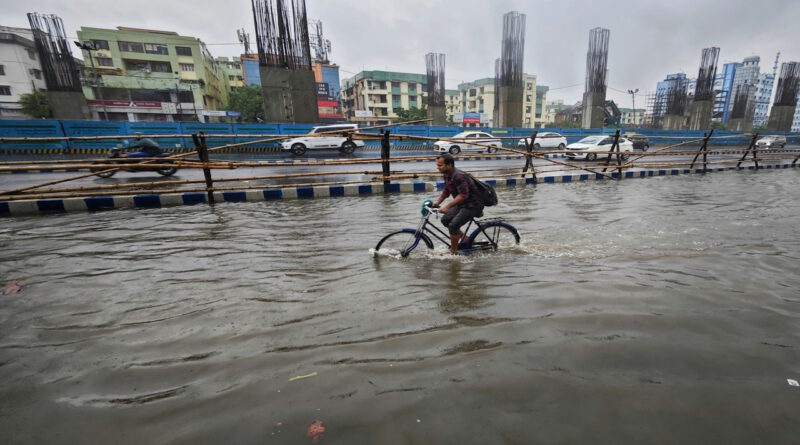 Mann fährt mit Fahrrad durch Wasser auf einer überfluteten Straße.